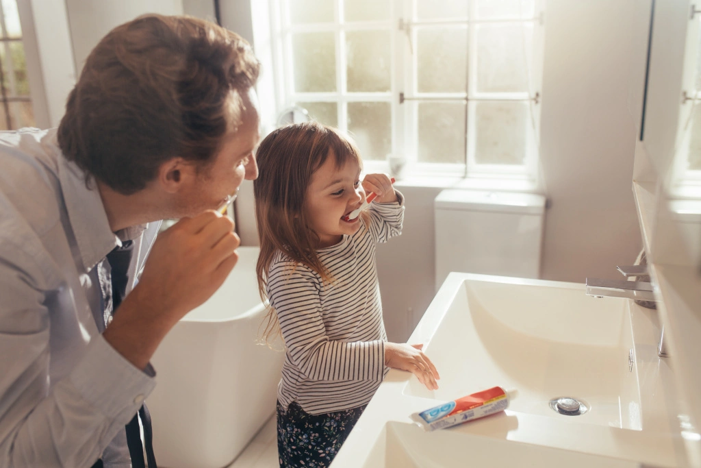Tato z córką myją wspólnie zęby w łazience przy umywalce