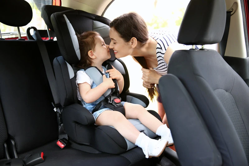 Dziewczynka w foteliku samochodowym dla dziecka bawi się z mamą