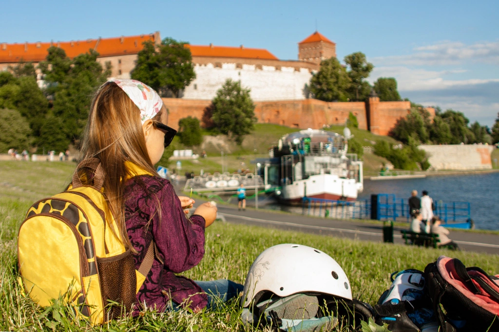 dziewczynka siedzi na bulwarach w Krakowie, w tle widać Wawel