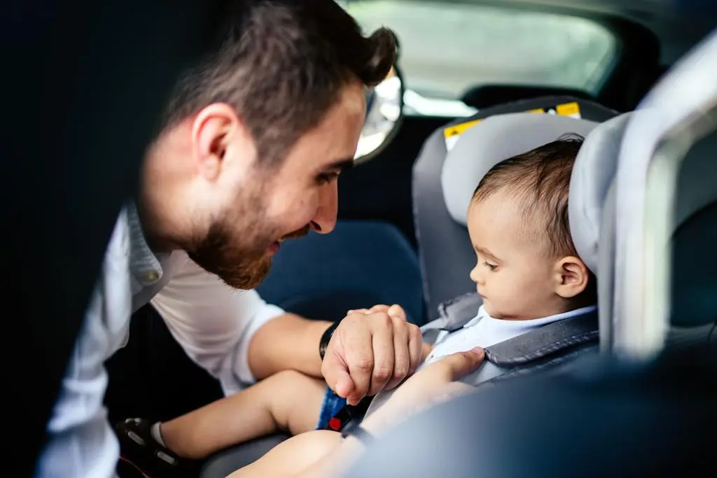 tata zapina dziecko w bezpiecznym foteliku samochodowym
