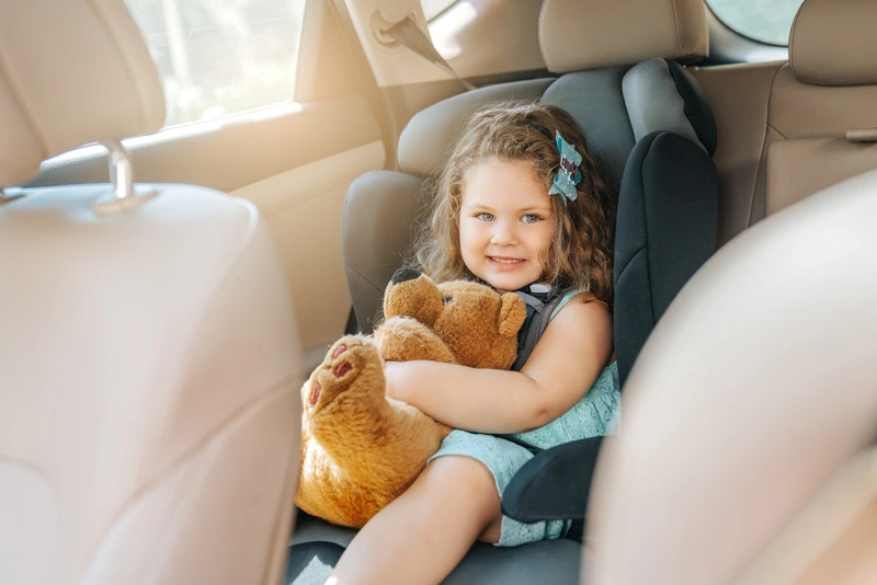 Dziewczynka w foteliku samochodowym dla dziecka przytula misia